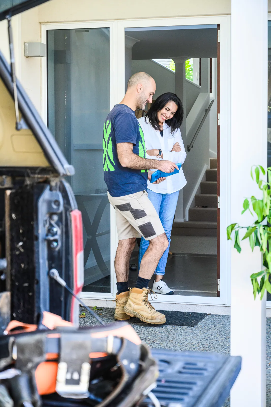 A tradie showing a homeowner something on a tablet at her front door