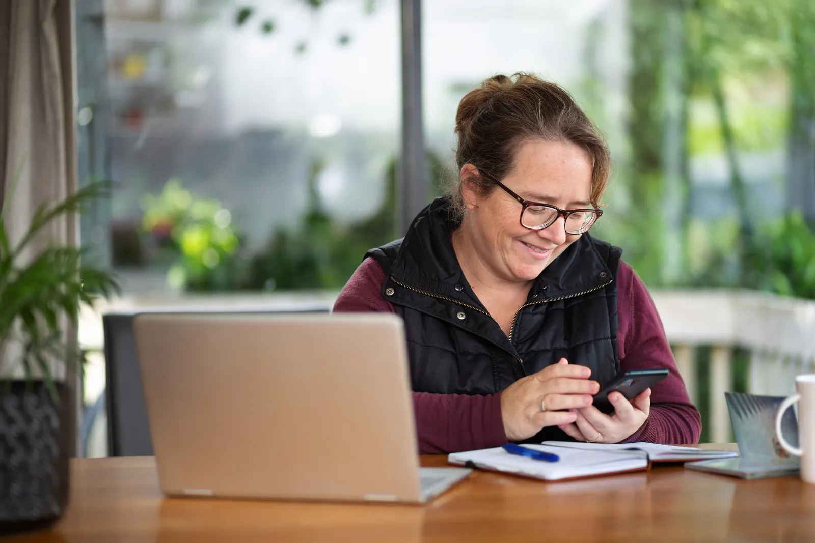 A woman smiling at her phone beside a laptop