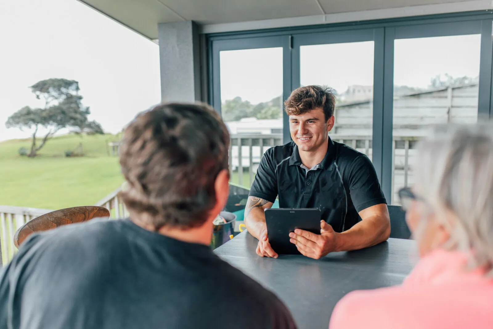 A young man with a tablet talking with customers at a table